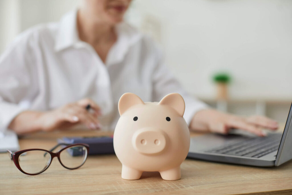 Piggy bank on desk with laptop and glasses.