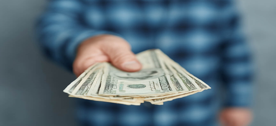 Hand holding out US dollar bills.
