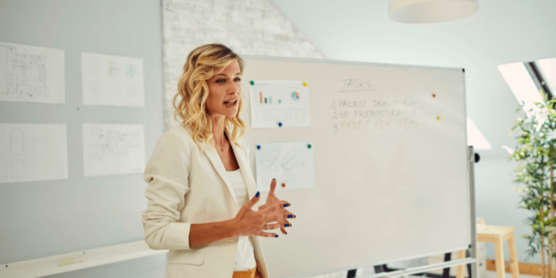 Woman presenting at whiteboard with charts and notes.