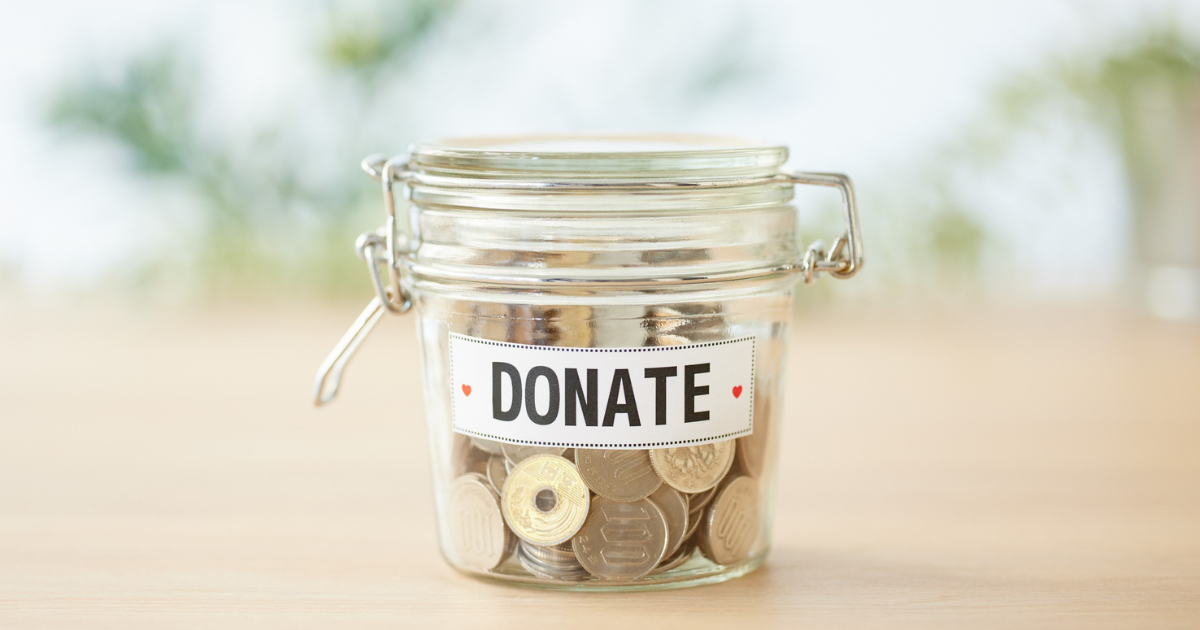 A glass jar full of coins and a sticker on the jar with the word donate on it.