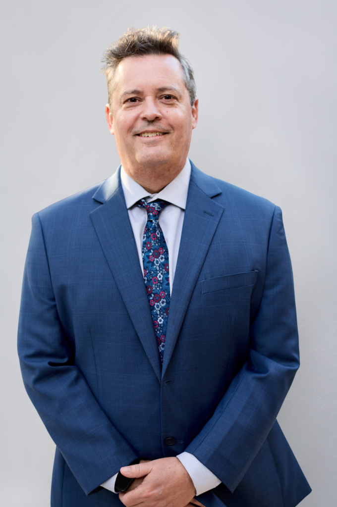 Man in blue suit smiling, white background.