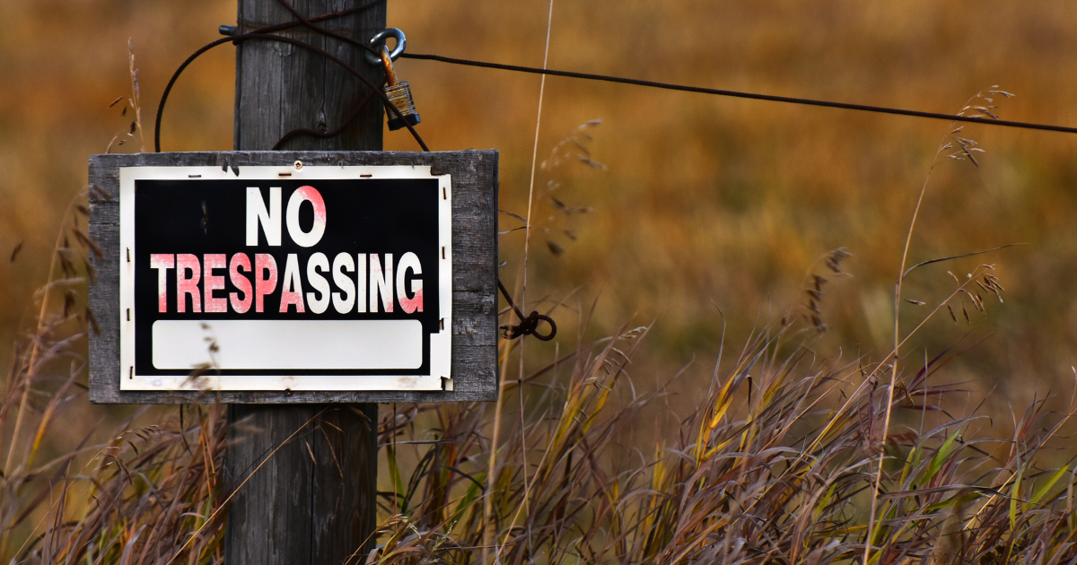 A wood fence in a field with a No Trespassing sign.