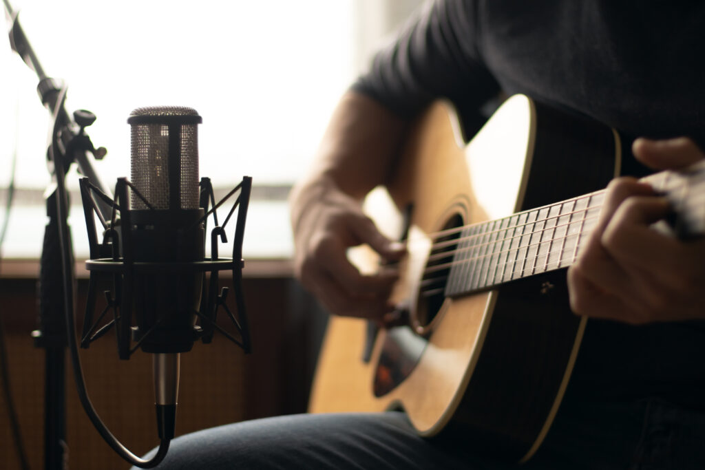 Man playing acoustic guitar and recording with a microphone in a home studio